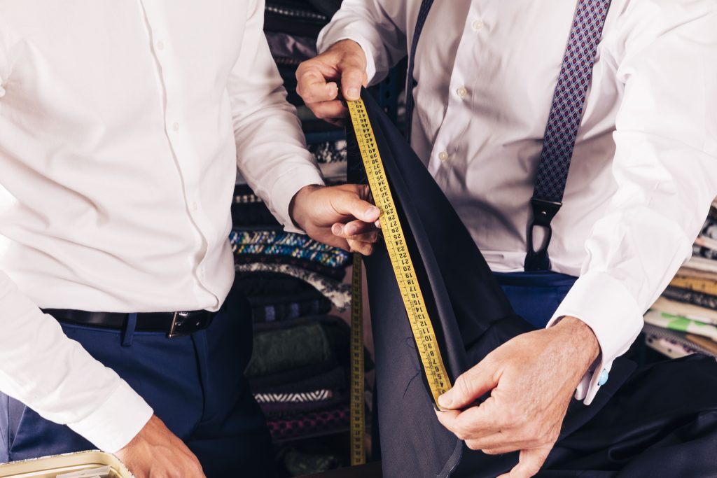 customer-senior-male-tailor-measuring-fabric-with-yellow-measure-table-min