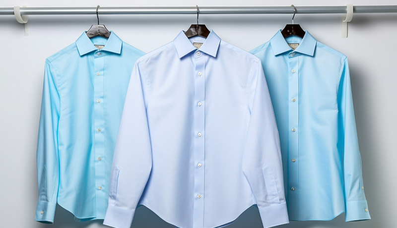 Three perfectly pressed, wrinkle-free blue dress shirts hanging on a rack, illustrating the crisp, professional standard maintained by expert laundry service.