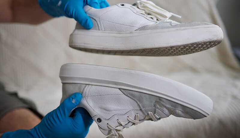 A ByNext technician using a specialized soft-bristle brush to deep clean the midsole of a white leather sneaker, demonstrating the professional restorative process.