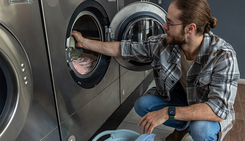 A man in a plaid shirt loading a large industrial washing machine at a professional laundry facility, illustrating the high-capacity equipment that provides a deeper clean than home units.