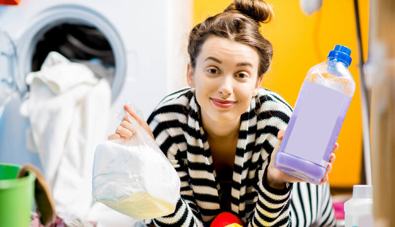 A woman in a striped shirt holding a bottle of purple liquid detergent and a bag of white powder, illustrating the choice betwee