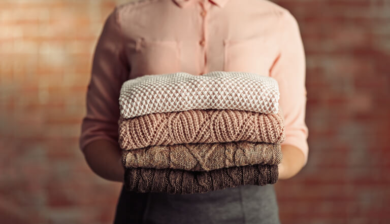 A stack of neatly folded cable-knit wool and cashmere sweaters after sweater dry cleaning.