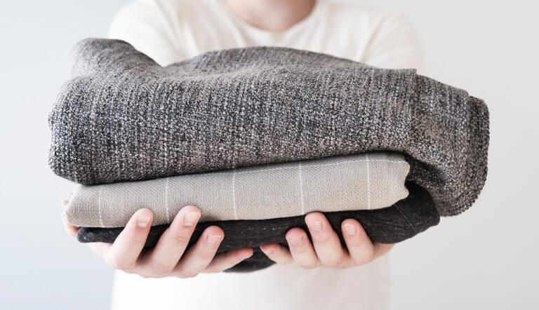 Hands holding a stack of folded wool and textured knit garments ready for professional sweater dry cleaning.